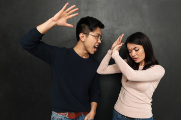 Worried asian woman covering himself while boyfriend trying to kick