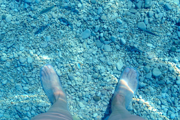 Naklejka premium under water view of feet and water shoes, fish and pebble