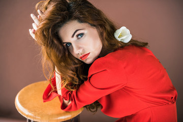 Naklejka premium Woman with long red hair with tulip flower leaning on stool isolated on brown background