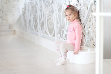 Pensive little girl sitting on the stairs. Bright interior in the house.