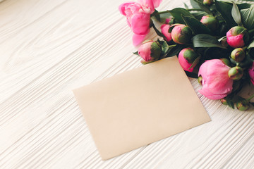 lovely pink peonies with empty craft card on rustic white wooden background top view, space for text. floral greeting card mock-up. beautiful flowers. happy mothers day concept