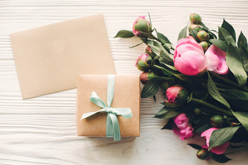 lovely pink peonies with empty craft card and gift box on rustic white wooden background top view, space for text. floral greeting card mock-up. happy mothers day concept