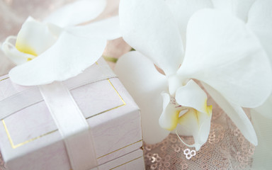 Gift box for decorations with an orchid flower against a shiny fabric background.