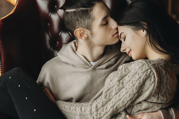 Close up portrait of a beautiful young couple sitting on a leather chair where boy is kissing his girlfriend on the forehead while she is smiling with closed eyes.