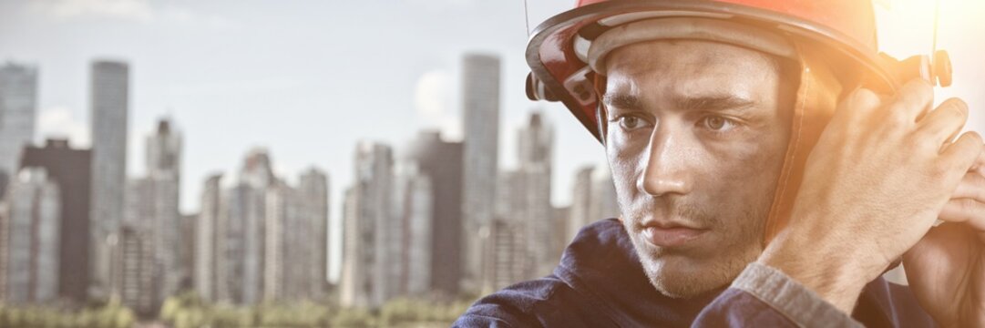 Composite image of serious fireman putting on helmet