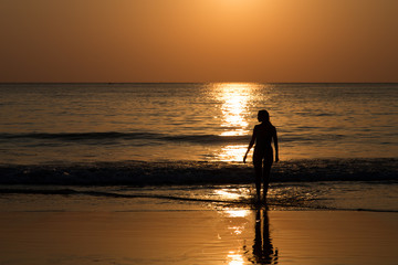 Fototapeta na wymiar Profile Silhouette of the young woman standing in the water during golden sunset. Image of A girl is ready to enter to the sea at sunset in Thailand