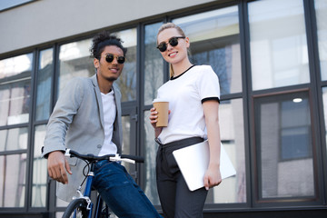 young multiethnic couple in sunglasses smiling at camera on street