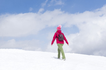 Fototapeta na wymiar girl in a red jacket and hat is on a snowy slope against the blue sky with clouds