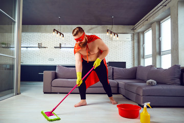 A fat, funny man in a superhero costume is cleaning the house. Cleaner is a super hero in the...