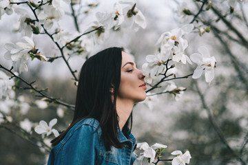 Young attractive slim woman wearing blue stylish jeans jacket posing over blossoming magnolia trees