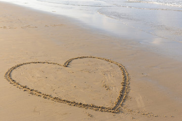 Fototapeta na wymiar Heart drawn on a sand beach with the sea in the morning.