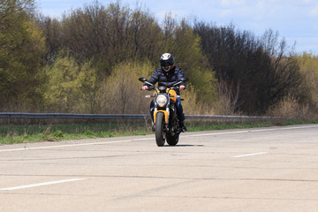 Obraz premium Male motorcyclist at the wheel of a racing motorcycle on a high-speed empty road. with pleasure passing an empty road to travel by motorcycle. Place for text, extreme sport, freedom concept