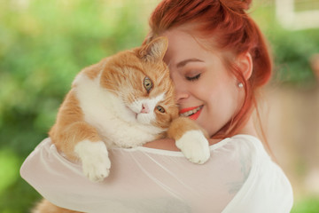 Beautiful young woman cuddling with cute red cat in her arms