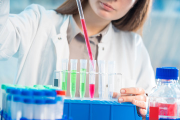 Fototapeta premium Young woman in scientific lab with pipette and chemicals in test tubes