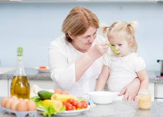 Senior woman feeding baby girl with a spoon at kitchen