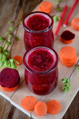 Red vegetable smoothie made of carrot and beetroot in glass jars on wooden background