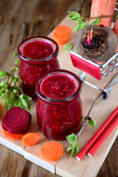 Red vegetable smoothie made of carrot and beetroot in glass jars on wooden background