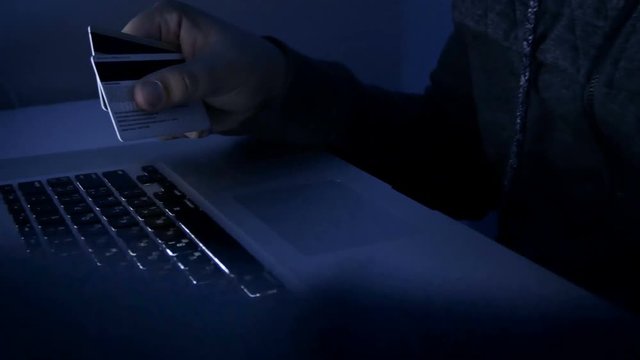 4k closeup footage of hacker holding credit cards typing code on laptop