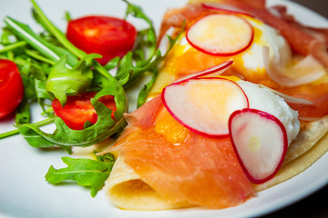 Eggs Benedict with hamoon, radish, cherry tomatoes and Olandes sauce on a white plate