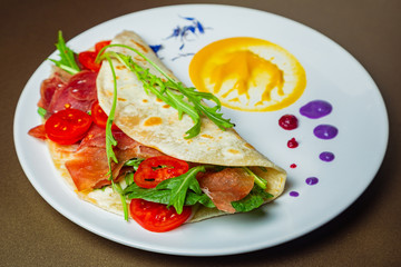 Piadina with chamoon, mozzarella, cherry tomatoes and arca on a white plate
