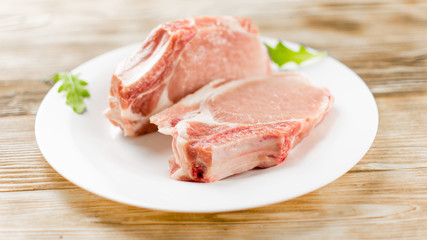Raw pork brisket, ribs on a white plate on a wooden background.