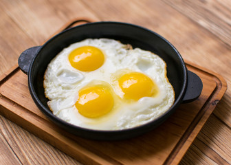 Fried eggs in a frying pan on a wooden background.