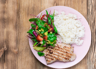 Grilled meat, boiled rice and vegetable salad on a wooden background.