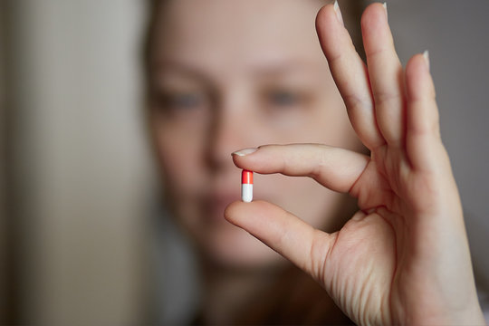 a young woman holds a red and white pill. Taking care of your health