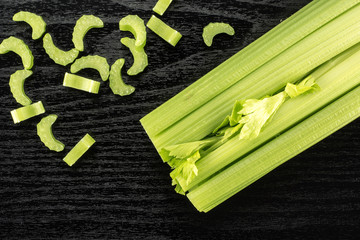 Fresh green celery with chopped pieces isolated on black wooden background.