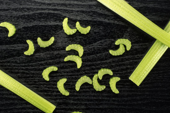 Three green celery sticks with fresh chopped pieces isolated on black wooden background.