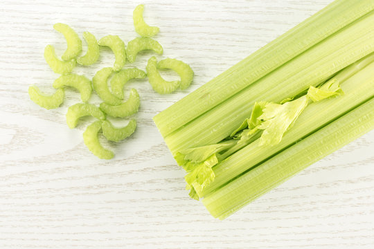 Fresh green celery with chopped pieces isolated on light wooden background.