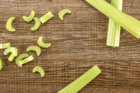 Three green celery sticks with fresh chopped pieces isolated on wooden background.