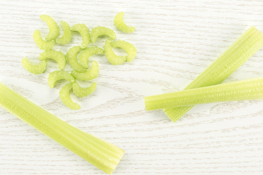 Three green celery sticks with fresh chopped pieces isolated on light wooden background.