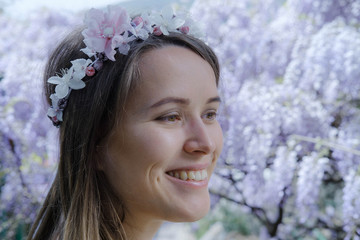 Young blonde curly hair woman in blooming wisteria garden in spring. Woman wearing in lilac dress © Boyarkina Marina