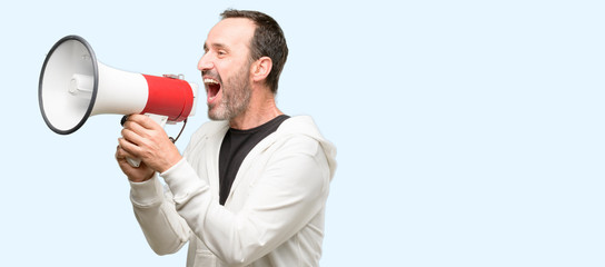 Middle age man wearing sportswear communicates shouting loud holding a megaphone, expressing success and positive concept, idea for marketing or sales isolated over blue background