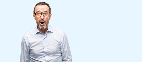 Middle age man with glasses scared in shock, expressing panic and fear isolated over blue background