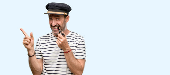 Sailor captain man smoking a tobacco pipe pointing away side with finger isolated over blue background