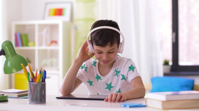 childhood, technology and leisure concept - smiling little boy with tablet pc computer and headphones listening to music at home