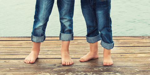 Two brothers stand barefoot on  the wooden pier .Family vacation on the lake.	
