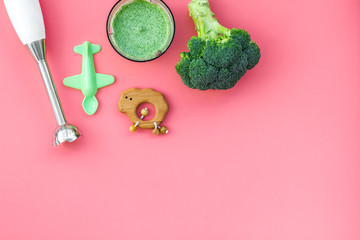 Homemade baby food. Cook puree with broccoli with immersion blender. Pink background with toy top view space for text