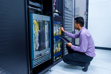 Network administrator with tablet computer in hand working with networking switch in data center room