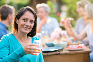 Looking at the camera a beautiful brunette woman in her forties with a wine glass by hand. She sits...
