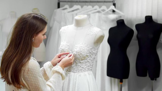 Portrait of a girl creating a wedding dress by exclusive order sewing fabrics and rhinestones on a dress dressed in a mannequin. production of wedding dresses. Little business