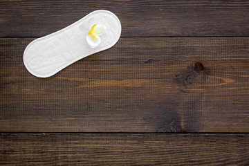 Women's hygiene products. Critical days concept. Sanitary pads near small flowers on dark wooden background top view copy space