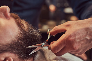 Professional hairdresser modeling beard with scissors and comb at the barbershop. - obrazy, fototapety, plakaty