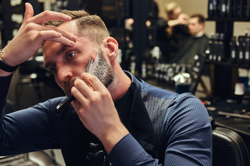 Portrait of a stylish male who himself shaving in a hairdressing salon.