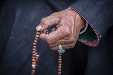 Old Tibetan woman holding buddhist rosary in Hemis monastery, Ladakh, India. Hand and rosary, close up