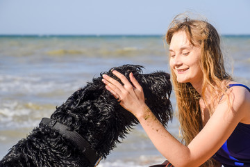 Blonde girl with a black curly dog on the beach.