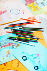 Pencil crayons scattered on desktop filled with colorful drawings