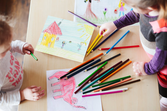 Little girls drawing a colorful pictures of elephant and playing children using pencil crayons standing at table. Shot from above